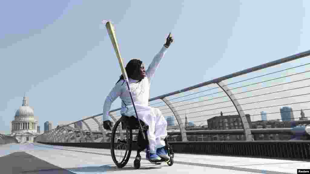Paralympian Ade Adepitan waves to the crowd below as he carries the Olympic flame across the Millennium Bridge in front of St. Paul's Cathedral in London on July 26. (REUTERS/Luke MacGregor)