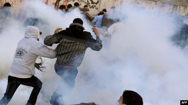A protester prepares to hurl a tear-gas canister back at security forces as others run for cover on the third day of clashes on Tahrir Square in Cairo on November 21.