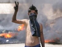 Smoke billows from burning tires as a Lebanese boy flashes the victory sign at a blocked road leading to the international airport in Beirut (AFP)