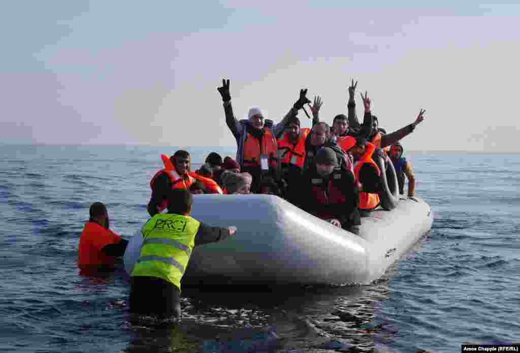 Syrian refugee Daoud Daoud, 20 (center), raises his gloved hands in triumph as his boat arrives on the beach at Lesbos, Greece.