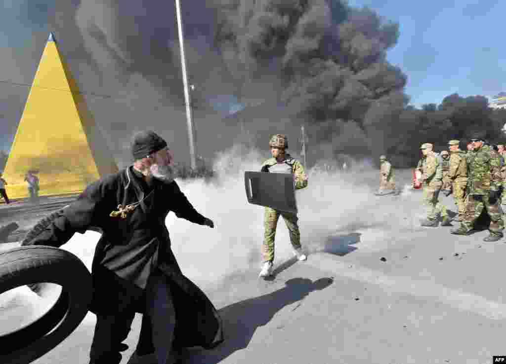 An Orthodox priest throws a tire as "Maidan self-defense" activists clash with fighters of the volunteer Kyiv Battalion on Independence Square in Kyiv on August 7. (AFP/Sergei Supinsky)