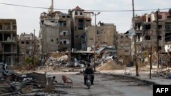 A man drives his motorbike past damaged buildings in Harasta, east of the Syrian capital, Damascus, on February 10.