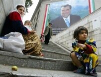A mother and child begging under a portrait of Tajik President Emamali Rahmon (AFP)