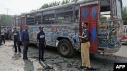 A policeman and volunteers stand in front of a damaged bus after a bomb explosion in Karachi on August 17.
