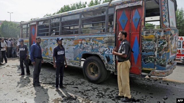 A policeman and volunteers stand in front of a damaged bus after a bomb explosion in Karachi on August 17.