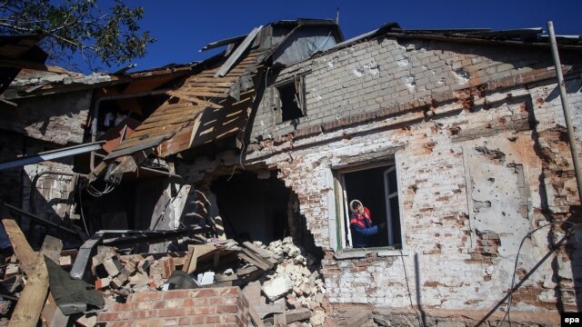 Село Пески: женщина смотрит в окно дома, разрушенного в результате обстрелов