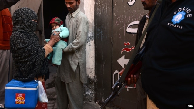 A Pakistani policeman stands guard as a polio-vaccination worker marks a child after immunization with antipolio drops in Lahore on December 21.