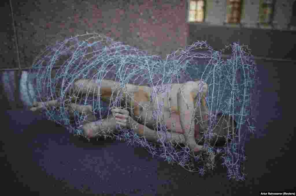 Russian artist Pyotr Pavlensky lies on the ground, wrapped in a roll of barbed wire, during a protest in front of St. Petersburg's Legislative Assembly. (Reuters/Artur Bainozarov)