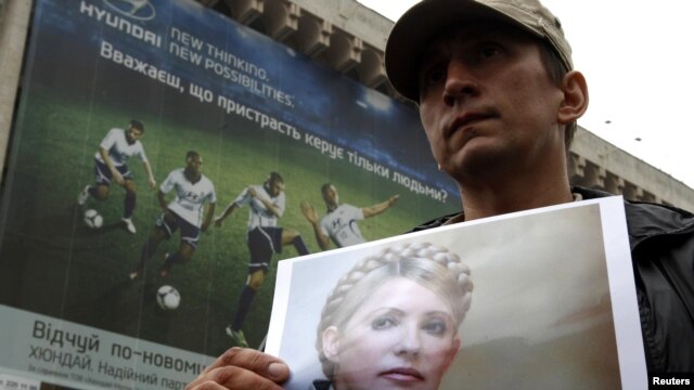 An opposition supporter holds a photo of former Prime Minister Yulia Tymoshenko in front of a billboard for Euro 2012 in Kyiv.