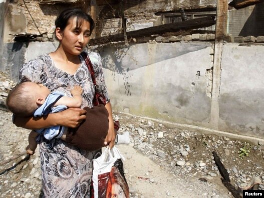 An ethnic Uzbek woman and her child, just returned to Osh from Uzbekistan, walks past a house that was burned down during ethnic clashes.