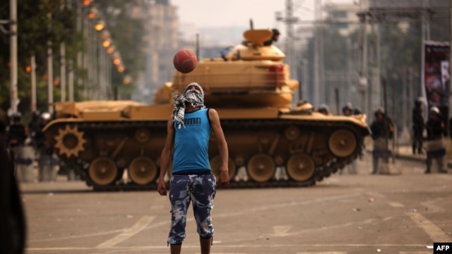 An opposition supporter plays football next to a Republican Guard tank deployed outside the presidential palace in Cairo.