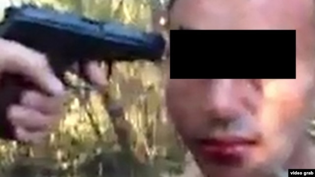A screen shot from a video purportedly showing a man being threatened at gunpoint while being forced to sodomize himself with a bottle.