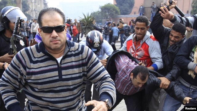 Egypt -- A plainclothes policeman (L) runs to attack a foreign journalist during a demonstration in Cairo, 28 January, 2011