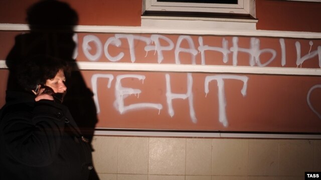 A man walks past graffiti spray-painted on the building used by the Memorial human rights group. It reads: "Foreign agents. I love USA."