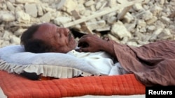 A survivor of the Balochistan earthquake sleeps near the rubble of his mud house.