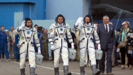 «Soyuz TMA-18M» ğarış kemesi ekipajınıñ müşeleri (soldan oñğa): qazaqstandıq Aydın Ayımbetov, reseylik Sergey Volkov jäne daniyalıq Andreas Mogensen. Bayqoñır, 2 qırküyek 2015 jıl.