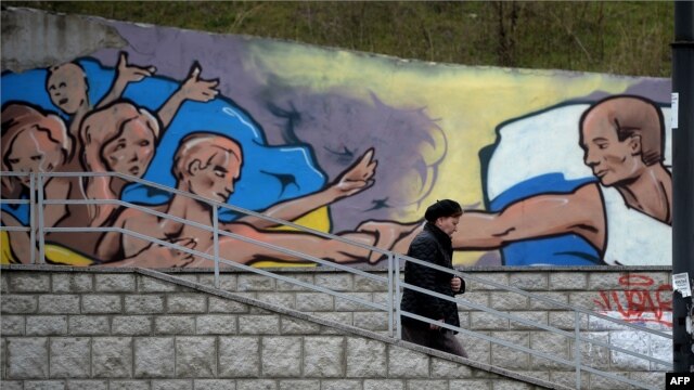 A woman in Simferopol walks past a mural depicting Russian president Vladimir Putin giving a hand to  Ukranians. 