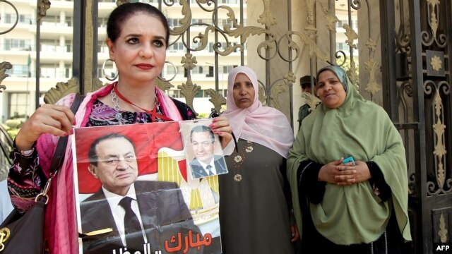 A woman holds a poster of ousted president Hosni Mubarak as she stands outside the military hospital where he was transfered after suffering a stroke in prison in Cairo.