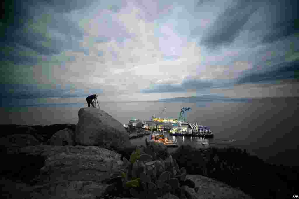 A photographer takes pictures of the "Costa Concordia" cruise ship off the Italian island of Giglio. Work is moving head to remove the ship almost a year after it ran aground, killing 32 people. (AFP/Filippo Monteforte)