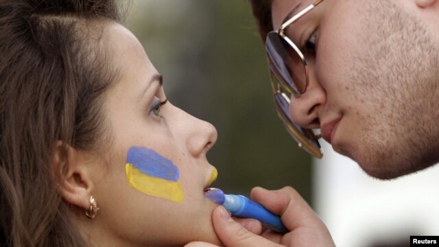 A man paints the colours of the Ukrainian national flag on a woman's face at the Euro 2012 fan zone in Kharkiv.
