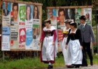 Germans in traditional Bavarian dress walk past campaign posters