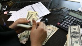 A woman counts US dollars banknotes in a currency exchange office in Tehran