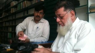 Haji Rasheed (right) bags a book for a customer in front of the dwindling stock of books at his Maktaba-e Sarhad bookstore in Peshawar.