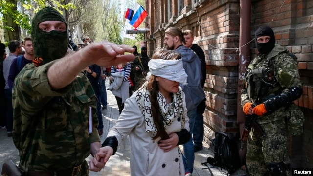 Сепаратист ведет Ирму Крат с завязанными глазами после пресс-конференции в Славянске, 21 апреля 2014 года