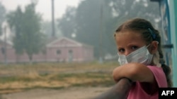 A girl wearing a protective mask looks out from her balcony in the village of Beloomut, near Moscow, during serious forest fires caused by a heat wave in 2010.