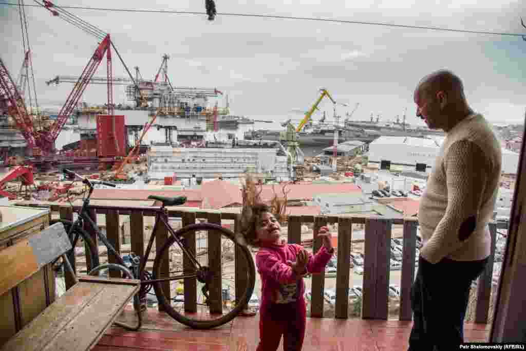 Janbulat Asperov watches his granddaughter play on the balcony of his house near the Bibi Heybet mosque.