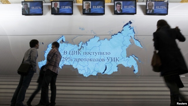 People stand near screens displaying preliminary results of the presidential elections at Vladimir Putin's campaign headquarters in Moscow on March 4.