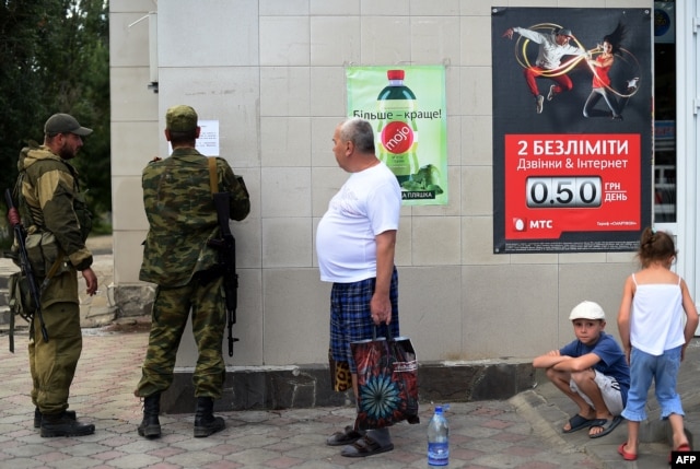 A separatist attaching a leaflet on a supermarket wall in Novoazovsk ~