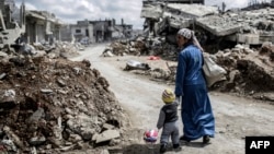 A Kurdish Syrian woman walks with her child past the ruins of Kobani after Islamic State militants had been pushed out of the town earlier this year.