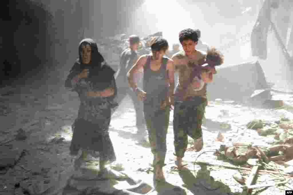 A Syrian woman and youths, one of them carrying a wounded baby, flee the site of a reported barrel-bomb attack by Syrian government forces in the northern city of Aleppo on June 26. (AFP/Zein Al-Rifai)