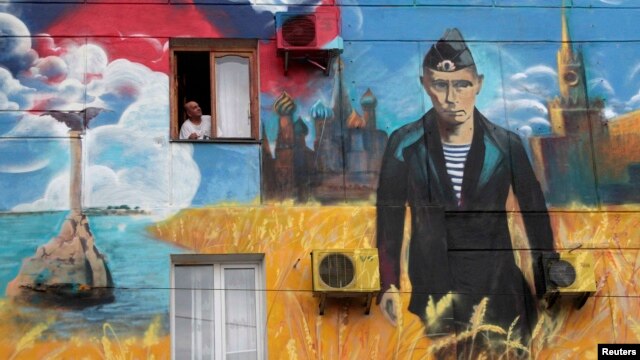 Житель Севастополя выглядывает из окна, в стена его дома украшена политическим настенным рисунком. Май 2014 года