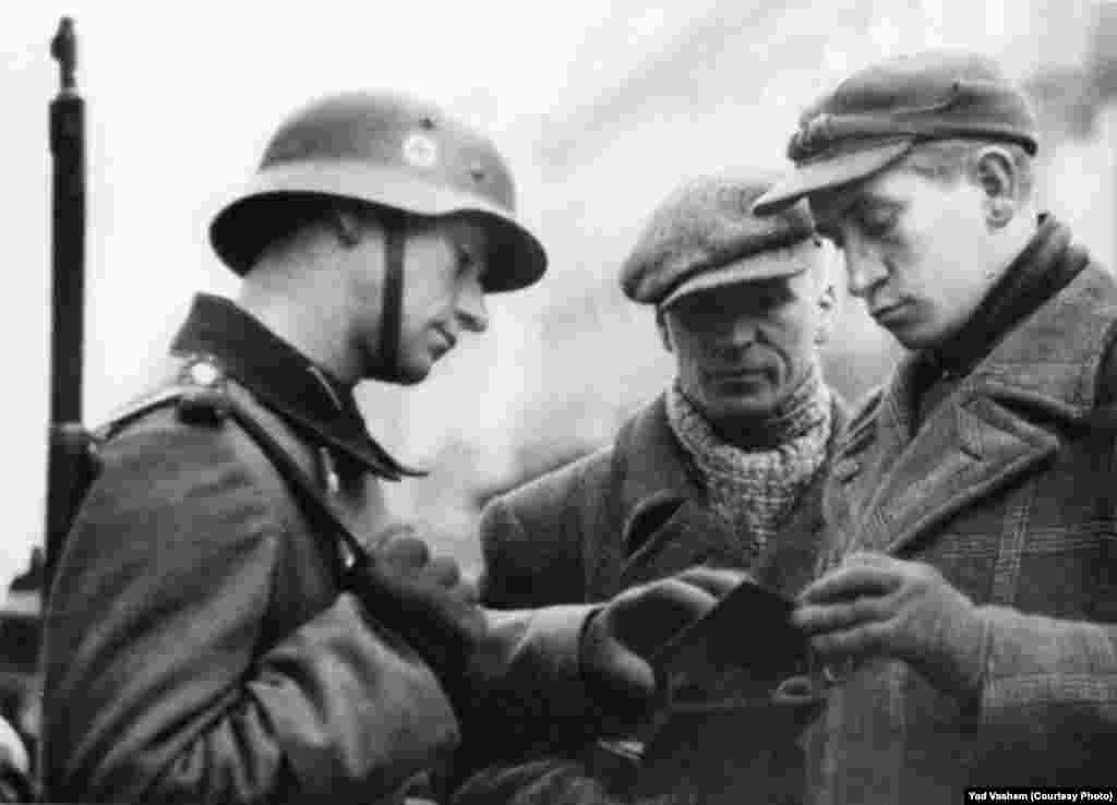 A German soldier checks the documents of two Jews.
