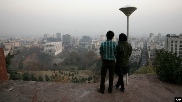 A couple stands at a viewpoint overlooking Tehran, which is covered in smog.