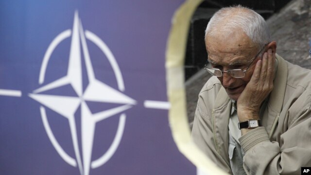 Beograd: Protestant protiv NATO-a iza postera sa znakom Alijanse, jun 2012.
