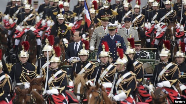 French President Francois Hollande (center left) stands to attention in a command car as he reviews  troops on the Champs-Elysees in Paris at the start of the traditional Bastille Day military parade. 
