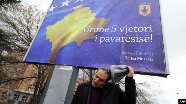 Un etnic albanez în faţa unui billboard cu inscripţia "La Mulţi Ani Kosovo, cu ocazia celei de a cincea aniversări a independenţei", la Pristina, 13 februarie 2013