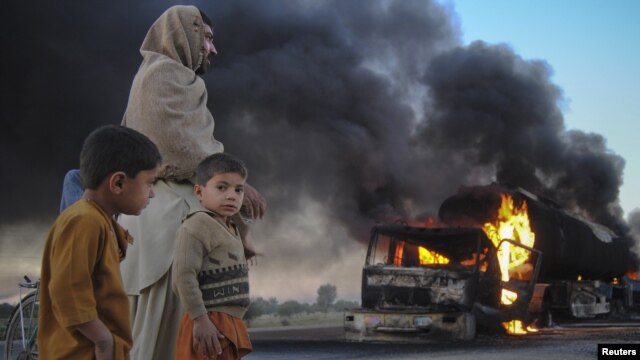 Pakistanis watch fuel trucks that were set ablaze in the Bolan district of Baluchistan Province on December 12.