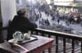 A man watches the market crowd from the second floor of a teahouse.