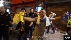 A pro-democracy protester wearing goggles to protect his eyes from chemical agents gestures as police advance toward him and other demonstrators during clashes on a street in the Mongkok district of Hong Kong early on October 19.