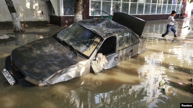 A local resident passes by a damaged car stuck in a flooded street in the town of Krymsk in Russia's Krasnodar region.