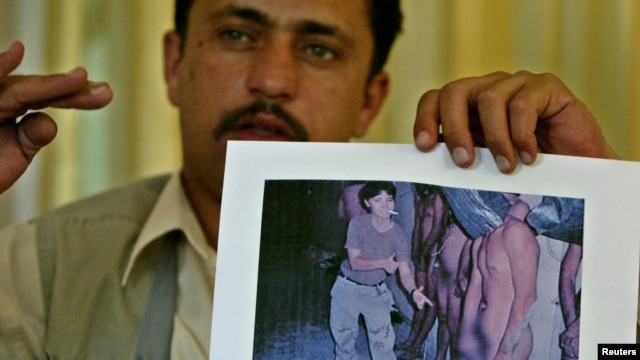 Saddam Saleh, a former prisoner at Abu Ghraib, shows a photograph at a 2004 press conference from the scandal that includes him in the middle of a group of naked prisoners being mocked by Lynndie England.