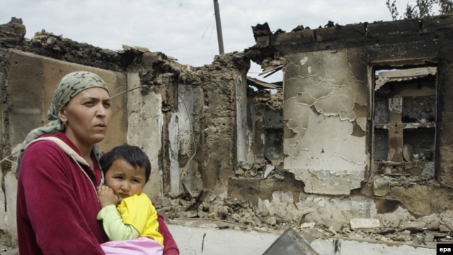 An ethnic Uzbek woman on June 16 carries her child past homes destroyed during the clashes in her village, Kyr-Aryk in the Osh region.