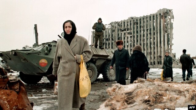 Chechnya -- Chechen women and men pass by a Russian armoured personnel carrier in front of the destroyed presidential palace in Grozny.  Feb1996.