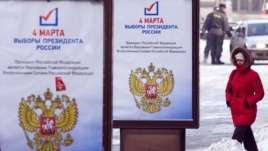 A woman passes by a presidential election campaign posters in Moscow
