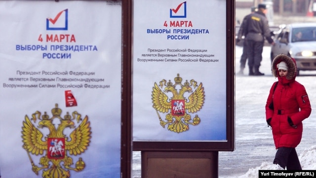 A woman passes by a presidential election campaign posters in Moscow
