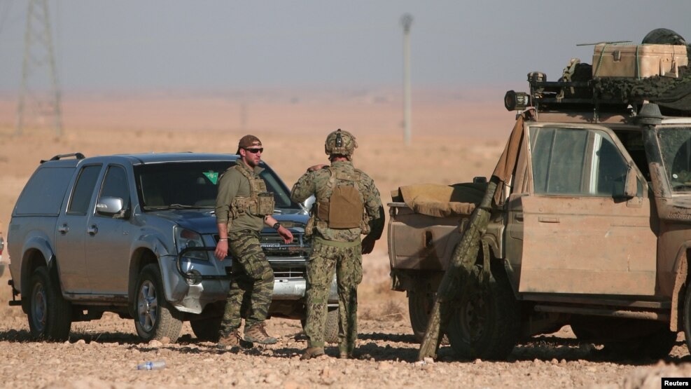 U.S. servicemen stand near military vehicles, north of Raqqa, in Syria earlier this month